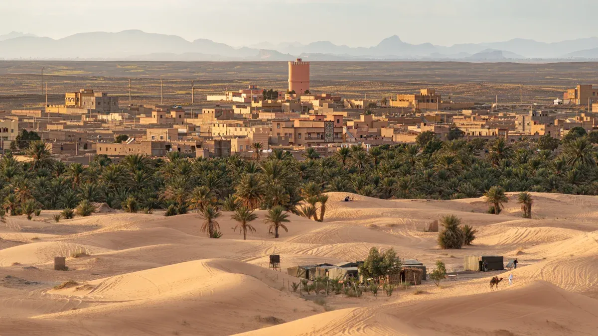 Merzouga village among palms with Erg Chebbi dunes in front on a Morocco tour package, Merzouga village, Morocco